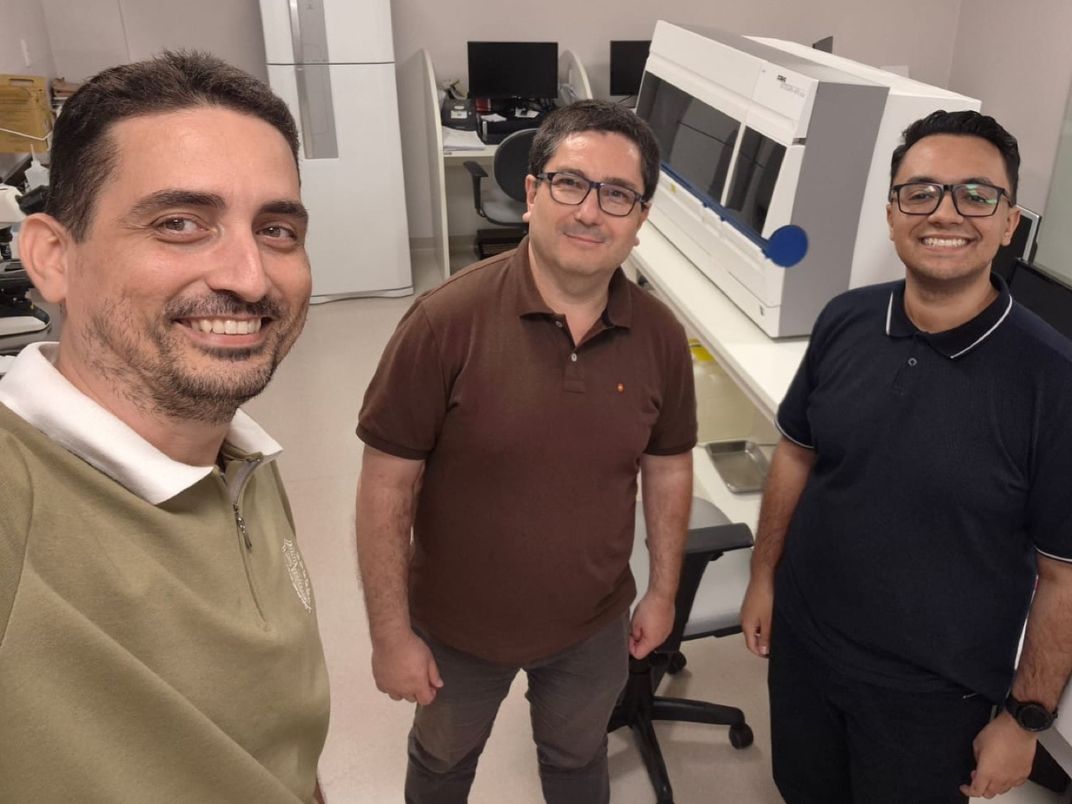 Três integrantes da equipe KognoVIA sorrindo, em pé, no laboratório de um cliente